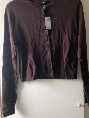 Brun kofta XS från 157 - Mysig brun kofta från 157 i storlek XS. Koftan har rund halsringning, långa ärmar och stängs med knappar framtill. Tillverkad i mjuk bomull som passar perfekt till lager på lager under höst och vinter.