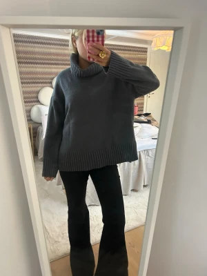 Mörkgrå stickad polotröja - Säljer en oversized mörkgrå stickad polotröja med bred ribbstickad kant vid ärmslut och nederkant. Tröjan har hög, mysig polokrage och långa ärmar. Perfekt för kyliga dagar och enkel att styla med jeans eller kjol.