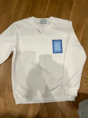  Casablanca hoodie - Säljer en clean vit sweatshirt från Casablanca med blå grafiskt tryck både fram och bak där det står 'Casa Blanca'. Tröjan har rund hals, långa ärmar och ribbade muddar. Perfekt för dig som gillar stilrena plagg med en twist. Säljer den eftersom den är liten i storlek 