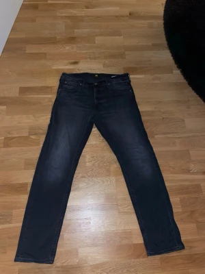 Svarta Lee jeans straight fit - Säljer ett par svarta jeans från Lee med klassisk femficksdesign och raka ben. Storleken är 34/32 Jeansen har Lee-logga på bakfickan och knapp, samt subtila slitningar för en snygg look. Jeansen är använda endast 1 gång och är i perfekt skick! Perfekta till vardags och passar till det mesta.