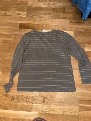Randig långärmad topp från H&M - En enkel och stilren långärmad topp från H&M Basics i beige med tunna vita horisontella ränder. Toppen har rund halsringning och är gjord i mjuk bomull, perfekt för en avslappnad look.