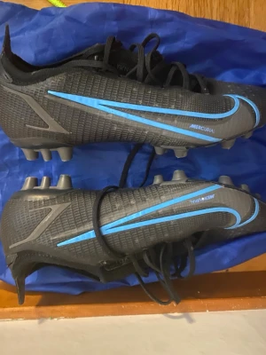 Nike svarta fotbollsskor med blå detaljer - Säljer dessa fotbollsskor storlek 40 elite. Skorna har inte använts mycket och är exklusiva och går inte att köpa pris kan diskuteras 