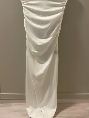 Vit och svart långklänning med drapering - Säljer två klänningar i vit och svart med snygg drapering längs sidorna. Klänningarna har en rak, elegant siluett och är sydda i ett mjukt, följsamt material som ger ett lyxigt intryck. Perfekt för dig som vill ha en stilren look med det lilla extra.