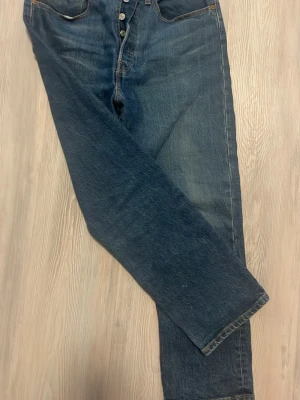 Levi's 501 Premium blå jeans - Klassiska Levi's 501 Premium jeans i mörkblå tvätt med raka ben och knappgylf. Jeansen har fem fickor, kontrastsömmar och den ikoniska läderlappen bak i midjan. Tillverkade i slitstark bomullsdenim som ger en tidlös look.