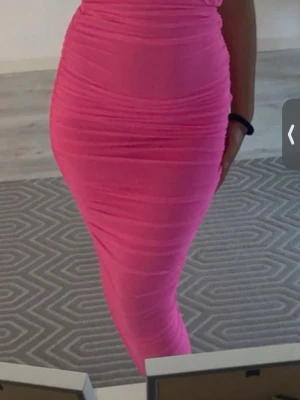 Tight rosa långklänning - Säljer en superfin långklänning i stark rosa färg. Klänningen är figurnära och har en snygg rynkad effekt längs hela kroppen. Perfekt för dig som vill sticka ut och ha en trendig look.