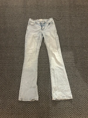 Ljusblå lowaist bootcut jeans från Gina tricot - Säljer ett par ljusblå jeans från gina i storlek 34. Byxorna har klassisk femficksdesign, dragkedja och knapp framtill samt bootcut-ben som ger en snygg retrovibe. 