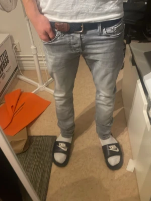Ljusgrå slim jeans med tvättad look - Säljer ett par ljusgrå jeans med tvättad effekt och klassisk femficksdesign. Jeansen har smal passform och raka ben, tillverkade i mjukt bomullsmaterial. Perfekta för dig som gillar en clean och avslappnad stil.
