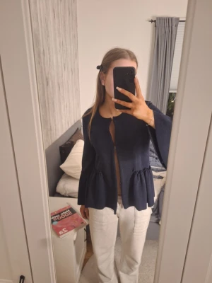 Mörkblå overshirt från Rosebud - Säljer en mörkblå overshirt från Rosebud i storlek S. Jackan har volangdetaljer vid ärmslut och midja, rund halsringning och är öppen framtill utan knäppning. Materialet är strukturerat och känns mjukt och bekvämt. Perfekt för dig som gillar en unik och trendig look.