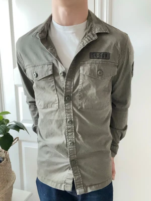 Superdry overshirt  - Superdry overshirt med loggor på bröstet och axeln. Väldigt snygg och väldigt najs passform! Inga defekter och sittter lite stort på modellen som är 180 cm 75 kg och bär storlek L! 