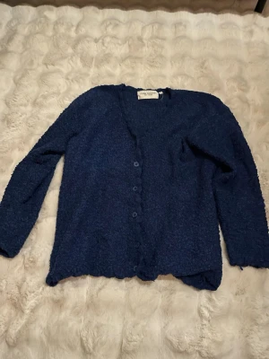 Mörkblå kofta från Lindex Collection - Mysig mörkblå kofta från Lindex Collection med knappar framtill. Koftan har lång ärm och är gjord i ett mjukt, strukturerat material som känns riktigt skönt mot huden. 