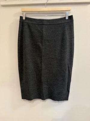 Mörkgrå pennkjol - Snygg mörkgrå pennkjol med klassisk rak passform och diskret dragkedja bak. Perfekt till en enkel topp eller stickad tröja för en clean look.