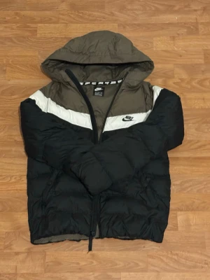 Nike pufferjacka med huva - Säljer en riktigt fet pufferjacka från Nike med huva. Jackan är svart med olivgröna och vita detaljer, har dragkedja framtill och är perfekt för kalla dagar. Klassisk Nike-logga på bröstet och skön passform som håller dig varm. Storlek 158-170 funkar för storlek S också 