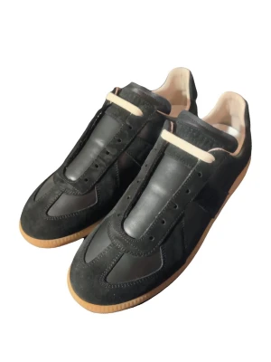 Maison margiela svarta. - Säljer ett par svarta sneakers från Maison Margiela med ovandel i både skinn och mocka. Skorna har en klassisk siluett, beige innersida och gummisula i naturfärg. Perfekta för dig som gillar stilrena och tidlösa sneakers med premiumkänsla.