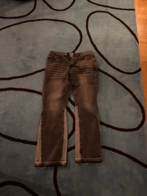 Denim Gallery Dept. bootcut jeans med rå kant - Unika bootcut jeans från Gallery Dept. i mörkgrå tvätt med ljusare paneler längs benen. Jeansen har råa, fransiga benslut och klassisk femficksdesign. Materialet är robust denim och passformen är loose med breda ben. Perfekta för dig som vill sticka ut med en edgy look.