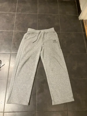 Grå mjukisbyxor från Arc'teryx - Säljer ett par grå mjukisbyxor från Arc'teryx med dragsko i midjan och raka ben. Byxorna har två sidofickor och en liten logga på vänster lår. Perfekta för chill dagar eller träning.
