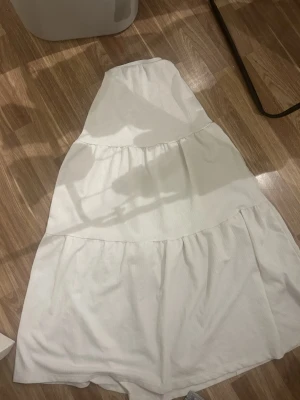 Vit långkjol från Gina Tricot XXS - Ljuvlig vit kjol med vackra volanger och bekväm resår i midjan. Den luftiga modellen ger ett feminint fall och passar perfekt för varma sommardagar, semester eller en avslappnad men stilren look. Lätt att matcha med både linne, blus eller stickad tröja beroende på säsong.  ✨ Bekväm passform ✨ Tidlös vit färg ✨ Perfekt till både vardag och fest  Ett måste i garderoben för dig som älskar enkla, fräscha plagg med det lilla extra 🤍