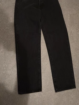 Svarta Supreme jeans straight fit - Supreme jeans i svart denim med klassisk röd Supreme-tag vid fickan och präglade knappar. Byxorna har rak passform och är tillverkade i 100% bomull för en skön och slitstark känsla. Perfekta för dig som gillar streetwear och vill ha en clean look.