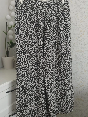 Svarta och beiga mönstrade byxor H&M - Säljer ett par luftiga byxor från H&M i storlek M. Byxorna har svart och beige abstrakt mönster, resår i midjan och är vida i modellen. Perfekta för dig som gillar bekväma och snygga byxor.