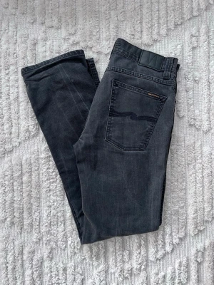 Nudie Jeans - Grå Svarta Nudie Jeans ”Slim Jim” i storlek W34 L34 men har måtten 43cm i midjan. Skicket är utmärkt