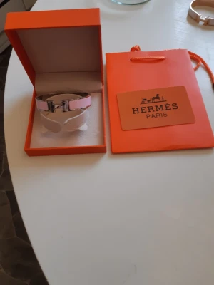 Hermes armband  - Bilderna visar ett Hermès-armband i rosa och silver med tillhörande ask och påse,