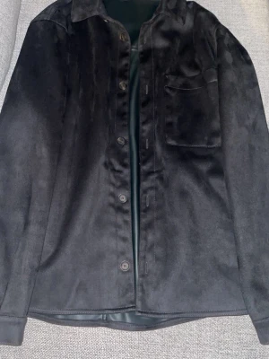 Svart overshirt i mocka-look - Snygg svart overshirt med mjuk mocka-känsla. Klassisk krage, knappstängning framtill och en bröstficka. Perfekt lager-på-lager-plagg för dig som gillar stilrena och minimalistiska outfits. Köpt på Zara. 