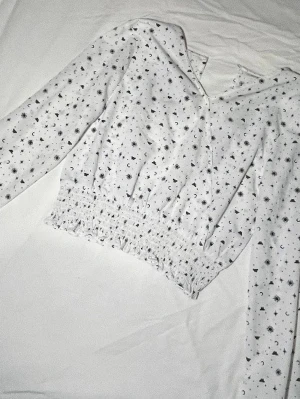 Vit blus med astrologiskt mönster Kappahl - Säljer en jättesöt blus från Kappahl i storlek 158 med svart astrologiskt mönster av solar, månar, stjärnor och fjärilar. Blusen har lång ärm och smockad, croppad midja! Passar till vardagen men även till speciella tillfällen!