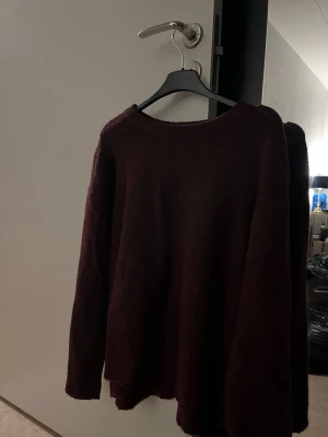 Mörkröd stickad tröja från 157 - Mysig mörkröd stickad tröja från 157 med rund halsringning och långa ärmar. Perfekt för kyliga dagar och enkel att matcha med jeans eller kjol. Tröjan har en klassisk passform och ribbade muddar vid hals och ärmslut.