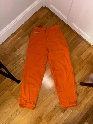 Orange baggy jeans från Cross Colours - Ett par asfeta orange jeans från Cross Colours. De har en loose och baggy passform, klassiska fem fickor och tydliga logopatchar både fram och bak. Robust bomull och skrikig orange. Väldigt statement, snygga