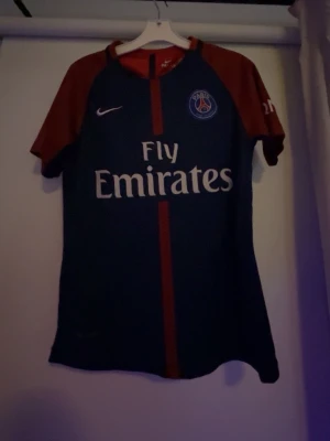 PSG Neymar Jr  barn matchtröja Nike 140 - Säljer en äkta Paris Saint-Germain matchtröja från Nike med Neymar Jr och nummer 10 på ryggen. Tröjan är marinblå med vinröda ärmar och röd rand framtill, tillverkad i Dri-FIT material för bästa komfort vid fotboll. PSG-logga och Fly Emirates tryck på bröstet. Tröjan är i barnstorlek 140.
