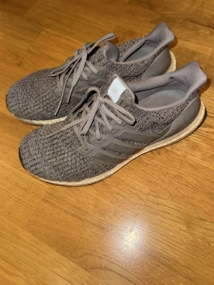 Adidas ultraboost grå - Säljer ett par grå adidas Ultraboost sneakers med stickad ovandel och snörning. Skorna har en platt sula med svart och vit mönstrad undersida, samt klassiska tre ränder på sidan. Perfekta för dig som gillar sportig stil och komfort. Storlek 42