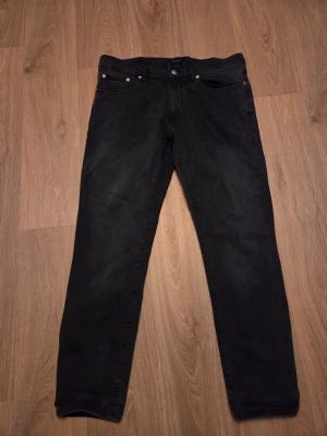 Svarta GANT Hayes Slim jeans W33/L32 - Svarta jeans från GANT i modellen Hayes Slim. Klassisk femficksdesign, smal passform och diskret GANT-logga på bakfickan. Tillverkade i mjukt bomullsmaterial med stretch för extra komfort. Perfekta för dig som gillar en clean och stilren look.