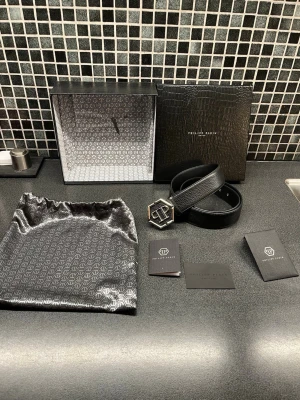 Svart skinnbälte från Philipp Plein - Exklusivt svart bälte från Philipp Plein i äkta skinn, tillverkat i Italien. Bältet har en unik hexagonformad metallspänne med PP-logga och en metallbricka med märkets namn och limited edition-detalj. Levereras med originalförpackning och dustbag med logomönster. Ny pris 5500kr pris går att diskutera. Mvh Oscar 