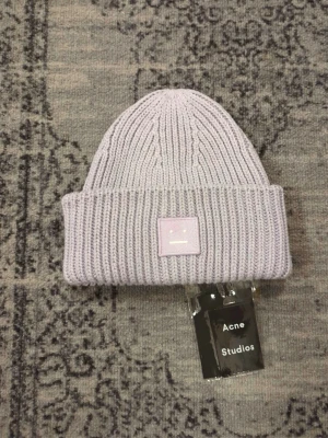 Ljuslila mössa från Acne Studios - Säljer en ribbstickad mössa från Acne Studios i en snygg ljuslila färg. Mössan är i 100% ull och har den klassiska Acne Studios-loggan framtill. Perfekt accessoar för att lyfta din look under kyliga dagar.