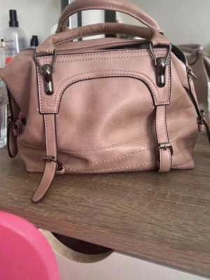Rosa axelväska i skinnimitation - Säljer en snygg rosa axelväska i skinnimitation med dubbla handtag och justerbar axelrem. Väskan har dragkedja upptill och en extra ficka med dragkedja på baksidan. Perfekt storlek för det viktigaste och stilren design.