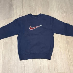 Mörkblå Nike vintagemjukisbyxor och tröja  - Säljer ett par vintage mörkblå mjukisbyxor från Nike med den klassiska röda och vita swoosh-loggan broderad på fickan. Byxorna har elastisk midja och muddar vid bensluten för extra komfort. Samt en vintage sweatshirt, båda i färgen marinblå/blå. Dom är i bra skick och i storlek S.