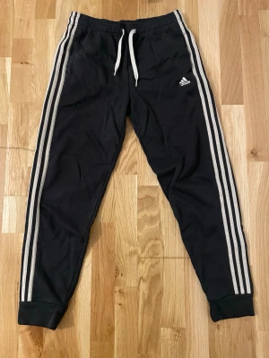 Adidas Mjukisbyxor - Säljer ett par bekväma Adidas mjukisbyxor i klassisk modell. De är gjorda i ett mjukt och skönt material som passar lika bra till träning som till hemmahäng. Byxorna är i princip i nyskick utan några hål eller fläckar. Självklart finns de ikoniska ränderna längs sidorna och loggan sitter snyggt på plats. En riktig klassiker som aldrig går ur tiden.