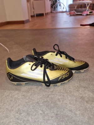 Adidas F50 Messi barn fotbollsskor guld - Säljer ett par ikoniska Adidas F50 Messi fotbollsskor i guld och svart med vita detaljer. 