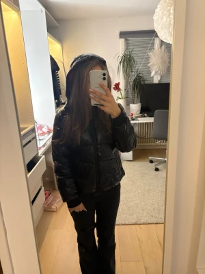 Svart pufferjacka från Calvin Klein - Snygg svart glansig pufferjacka från Calvin Klein med röd insida som håller värme jätte bra under kyliga vintrar. Jackan har en huva som går att sätta på och ta av. Säljer på grund av att den inte kommer till någon användning. Men mycket bra skick förutom lite smuts som inte syns pa längt avstand. Jackan är för barn även om det står storlek medium. Skulle säga att den är i kvinnostorlek XS - S beroende på hur du vill att den ska sitta. (Jag har storlek S på jackor)