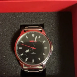 Hugo klocka i stål - (Äkta vara - Ord pris 1800)✨Stilren klocka från Hugo med svart urtavla och röda detaljer. Armbandet är i blankt rostfritt stål och klockan har minimalistiska indexmarkeringar. Passar perfekt till dig som gillar en clean och modern look.                   -Knappt i bruk helt ny fick julklapp förra året hitta den och säljer den nu. Följer med extra stålband till alla storklekar. 💬Vid snabb affär vid frågor och den skickas samma dag innan 22:00. 📬(1-3 dagars leveranstid)