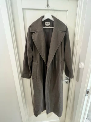 Grå kappa från Weekday i ullmix - Lång, grå kappa från Weekday med bred krage och dubbelknäppning framtill. Kappan har stora fickor, bälte i midjan och är helfodrad. Tillverkad i en mjuk ullmix som passar perfekt för kyliga dagar. Älskar denna och har bara haft den i 1 år men rensar garderoben :)