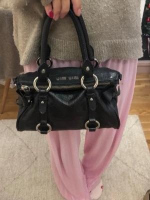 Miu Miu bow bag - Säljer den trendiga och sällsynta bow bagen ifrån miu miu. Det är en svart handväska i äkta skinn med dubbla handtag,silverfärgade detaljer runt hela väskan och rosetter på sidorna.Perfekt storlek för det viktigaste och riktigt snygg design, dessutom med ett fack inuti! Väskan är i super skick, däremot finns det en liten fläck på insidan, men som tur aldrig syns😊Köpt här på plick!!                             Storlek:Small Mått:ca 15x25