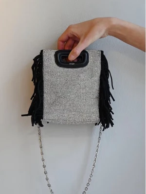 Maje crystal Embellished Bag - Säljer en svart maje väska som har en silver glittrig sida. Handtaget är i svart skinn och det tillkommer en avtagbar och justerbar axelrem i svart skinn, så du kan ha den runt axeln eller bara bära i handen😊Perfekt skick utan några defekter, pris kan diskuteras !silvriga kedjan tillkommer ej, bara det svarta bandet! De två sista bilderna är mina egna, de andra är lånade.                                           Storlek:mini Mått:17x16cm 