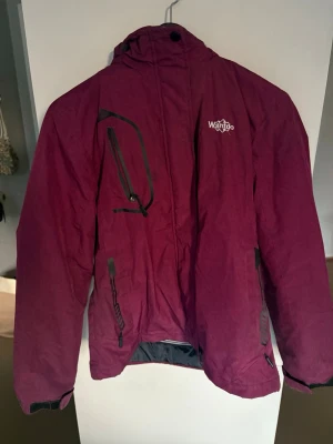 Vinröd skid/snowboard jacka,  Wantdo stor. S - Säljer en vinröd skidjacka från Wantdo med huva och flera fickor med dragkedja. Storleken är S. Fint färg men ändå lätt att se på backen. PBra skick, används 2-3 säsonger men är fortfarande i bra kondition. Jackan har en mjuk fleece insida och det går och ta bort huvan om man vill. 