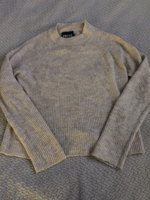 Beige stickad tröja från Pieces - Mysig beige stickad tröja från Pieces i storlek XS. Tröjan har rund halsringning, ribbade muddar och lång ärm. Perfekt för lager på lager under kyliga dagar och enkel att matcha med jeans eller kjol.