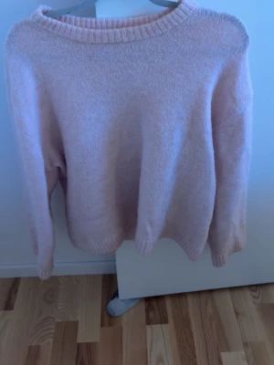 Ljusrosa stickad tröja Gina Tricot - Mysig ljusrosa stickad tröja från Gina Tricot i ullblandning. Tröjan har en relaxed, lite oversized passform med långa ärmar och ribbade muddar vid hals, ärmslut och nederkant. Perfekt för kyliga dagar och enkel att styla till jeans eller kjol.