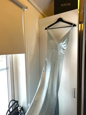 Ljusblå långklänning med snörning - Ljusblå balklänning i följsamt, stretchigt material som andas och formar sig vackert efter kroppen. Hudnära passform med dekorativ knytning i ryggen. Klänningen har ett längre släp baktill medan framsidan går ner över fötterna. Otroligt bekväm och elegant – perfekt för bal eller festligare tillfällen. 