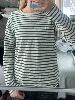 Randig långärmad t-shirt från Zara - Säljer en långärmad topp från Zara med gröna och vita horisontella ränder. Toppen har en rund halsringning och är gjord i mjuk bomull. Perfekt till jeans eller kjol för en chill look.