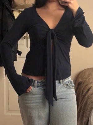 Svart omlottopp med knyt från Gina Tricot - Säljer en svart omlottopp från Gina Tricot i storlek M. Toppen har lång ärm, v-ringning och en snygg knytning framtill som ger en öppen detalj vid magen. Materialet är mjukt och stretchigt, perfekt att styla med jeans eller kjol.