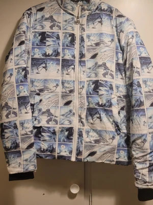 Blåvit vindjacka med serietidningsmönster - Säljer en unik vindjacka från Bossini i storlek S. Jackan har ett blåvitt serietidningsinspirerat mönster, dragkedja framtill och huva med snörning. Perfekt för dig som vill sticka ut med en cool och kreativ stil. Jackan är lätt och har svarta muddar vid ärmsluten.