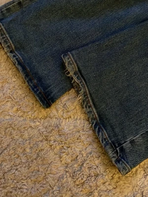Blå bootcut jeans - Säljer ett par blå jeans med bootcut passform och rå, fransig kant längst ner på benen. Jeansen har klassisk femficksdesign och är gjorda i ett slitstarkt denimtyg. Perfekta för dig som gillar en avslappnad och trendig look. Super fina🌺